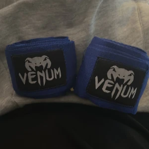 Venum boxningslindor - Säljer ett par blå boxningslindor från Venum. Perfekta för dig som tränar kampsport eller boxning och vill ha extra stöd för handleder och knogar. De är elastiska och har Venum-loggan i svart och vitt på kardborrebandet.