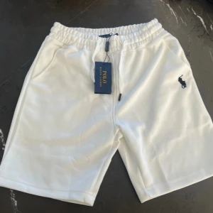 Vita shorts från Polo Ralph Lauren - Snygga vita shorts från Polo Ralph Lauren med elastisk midja och snörning. Klassisk design med Polo-logga broderad i mörkblått på ena benet. Perfekta för sommaren och chill dagar. Mjukt material som känns skönt mot huden.