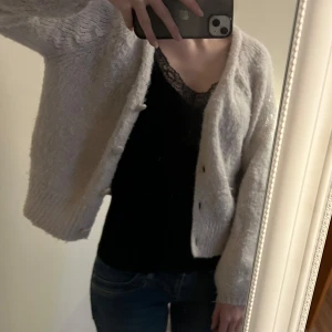 Beige stickad kofta med knappar - Mysig och fluffig beige stickad kofta med knappar framtill. Koftan har en lös passform, ribbade muddar och är långärmad. Perfekt att slänga över en topp för en chill och stilren look.