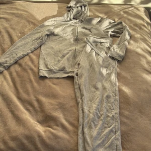 Grå mjukisbyxor från Puma - Säljer ett par grå mjukisbyxor från Puma med dragsko i midjan och ribbade muddar vid bensluten. Byxorna är i mjukt bomullsmaterial och har en enkel, sportig look med Puma-logga på benet. Perfekta för chill eller träning.