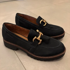 Mörkblå loafers - Snygga mörkblå loafers från Tamaris i mocka med chunky sula och guldfärgat spänne framtill. Använda ca 3 gånger så som nya🙌 (nypris 1200kr)
