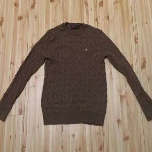 Brun kabelstickad tröja från Morris - Säljer en brun kabelstickad tröja från Morris i 100% merinoull. Tröjan har rund halsringning, lång ärm och en liten broderad logga på bröstet. Perfekt för dig som gillar klassisk och stilren look. Pris kan diskuter