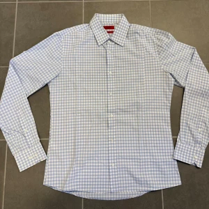 Blårutig skjorta från Hugo Boss - Snygg blårutig skjorta från Hugo Boss i slim fit-modell. Skjortan har klassisk krage, långa ärmar och knäppning framtill. Tillverkad i bomull för en skön känsla och stilren look. Perfekt för dig som gillar en fräsch och modern stil.