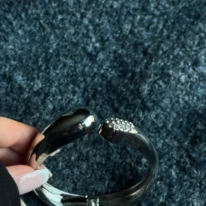 Silvrigt armband med glittriga stenar - Stilrent och chunky armband i silverfärg med en öppen design. Ena sidan är dekorerad med små glittrande stenar som ger extra bling. Perfekt för dig som gillar statement-smycken och vill sticka ut lite extra.