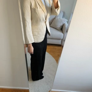 Kavaj - Cremefärgad glänsande kavaj i storlek 36. Fint skick. Liten slits vid ärmarna. Praktiska fickor på framsidan. Har tyvärr inte kvar märkeslapp men inköpt i Paris