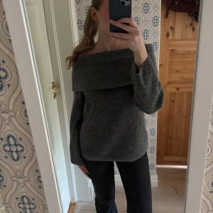 Grå offshoulder stickad tröja - Mysig grå stickad tröja med bred offshoulder-krage och långa ärmar. Perfekt för dig som gillar en avslappnad men ändå trendig look. Tröjan har en loose passform och är superenkel att styla till jeans eller kjol.