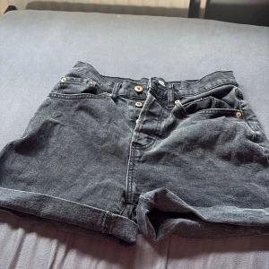 Svarta jeansshorts från - Snygga svarta jeansshorts från Lager 157 med hög midja och klassisk femficksdesign. Shortsen har uppvikta benslut och knappar i metall framtill. Perfekta för en chill sommarlook och lätta att matcha med allt.