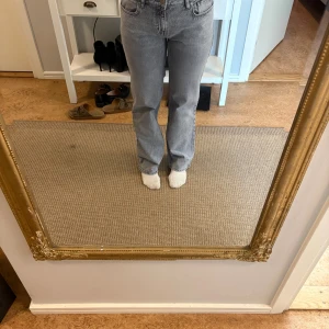 Grå raka jeans från NA-KD, Kate 28/32 - Säljer ett par grå jeans från NA-KD, modell Kate med raka ben och klassisk femficksdesign. Jeansen har normal midja och stängs med knapp och dragkedja. Perfekta för dig som gillar en enkel och stilren look.