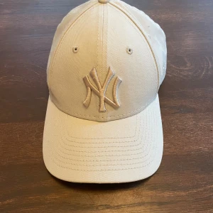 Beige New Era Yankees keps 9FORTY - Beige New Era 9FORTY keps med broderad New York Yankees-logga framtill. Justerbar rem baktill för perfekt passform. Kepsen är tillverkad i 100% bomull och har klassisk böjd skärm. Perfekt accessoar för en sportig och stilren look.