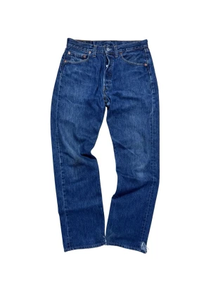 Levi's 501 blå jeans straight fit - Klassiska blå Levi's 501 jeans med rak passform och femficksdesign. Jeansen har knappgylf, normal midja och är tillverkade i slitstarkt denim av bomull. Snygga slitningar vid benslut för en avslappnad look. Perfekta till sneakers eller boots.