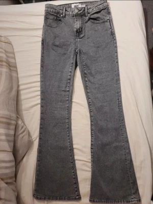 Grå bootcut jeans med broderade fickor - Säljer ett par grå bootcut jeans från 157 med snyggt broderade detaljer på bakfickorna. Jeansen har klassisk femficksdesign, bälteshällor och är tillverkade i mjukt denimtyg. Perfekta för dig som vill ha en retrovibe och cool siluett.