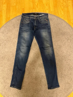 Replay Anbass blå jeans - Säljer ett par Replay Anbass jeans i klassisk blå tvätt med snygga slitningar och kontrastsömmar. Modellen har fem fickor och raka ben. Jeansen är tillverkade i mjukt denimtyg som sitter skönt hela dagen. Storlek: W29, L32. Vid funderingar eller liknande är det bara att höra av sig! 