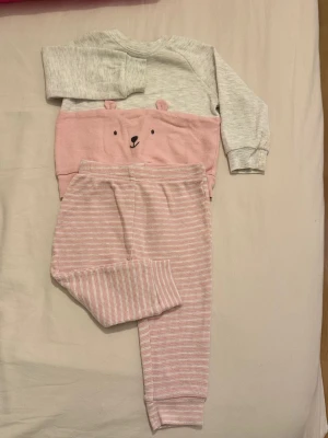 Grå och rosa randig babykläder Carter's - Supersöt väst från Carter's i grått och rosa med ett gulligt björnmotiv och små öron på framsidan. Den  är i mjuk bomull och har ett randigt mönster på byxorna. Perfekt för mysiga dagar hemma.