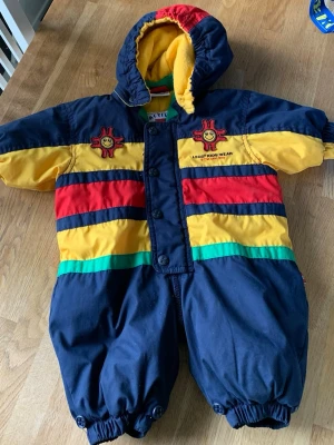 Färgglad overall från LEGO Kids Wear - Säljer en superfin overall från LEGO Kids Wear i storlek 58 för småttingar. Overallen har coola blockfärger i mörkblått, gult, rött och grönt, med broderade glada solar på bröstet. Fodrad med mjuk gul fleece och praktisk huva. Perfekt för kalla dagar!
