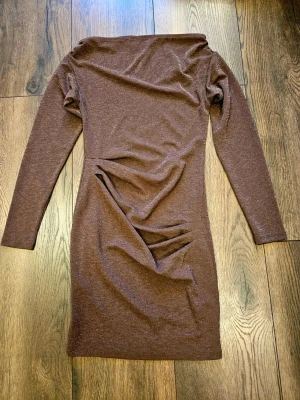 Brun glittrig klänning Kappahl  - Snygg brun glittrig klänning från Kappahl. Klänningen har lång ärm, figurnära passform och är tillverkad i ett stretchigt material med diskret glittereffekt. Perfekt för dig som vill sticka ut lite extra.