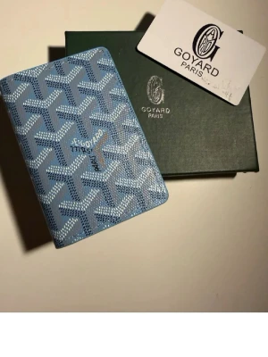Blå Goyard plånbok med mönster - Säljer en blå plånbok från Goyard med deras ikoniska grafiska mönster i vitt och mörkblått. Plånboken är kompakt och smidig, perfekt för kort och sedlar. Klassisk och stilren accessoar för dig som gillar exklusiva detaljer.