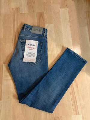 Replay Grover Hyperflex jeans blå - Säljer ett par Replay Grover Hyperflex jeans i klassisk blå tvätt. Modellen har rak passform (straight fit) och är tillverkad i stretchigt denim för extra komfort. Snygga detaljer med fem fickor och Replay-logga på bakfickan. Perfekta för dig som gillar stilrena och bekväma jeans.