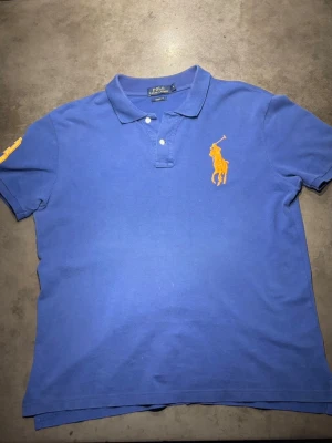 Ralph Lauren Pike - Säljer en riktigt snygg Blå pike från Ralph Lauren med orangea detaljer vid Ralph Lauren märkena. Storlek: L. Skriv vid frågor eller kom med bud!