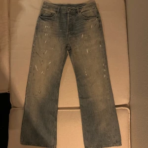 Acne Studios 2021m paint splatter jeans - Grå jeans från Acne Studios med raka ben och coola färgstänk och slitningar framtill. Klassisk femficksmodell med läderpatch bak i midjan. Materialet är 60% bomull och 40% lyocell för en mjuk känsla. Perfekta för dig som gillar en avslappnad och trendig look. Lite schysstare jeans helt enkelt. 