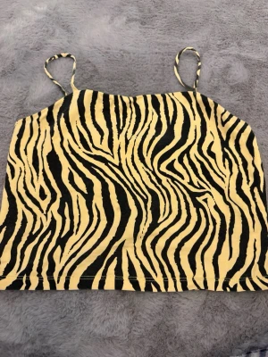 Zebramönstrad linnetopp XOXO Friends - Säljer en zebramönstrad linnetopp från XOXO Friends i storlek 146/152. Toppen har tunna axelband och är i gul och svart bomullsmix. Perfekt för dig som gillar djurmönster och vill sticka ut lite extra.