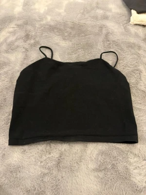 Svart croppad linnetopp - En enkel svart croppad linnetopp med tunna axelband. Toppen är rak i modellen och sydd i mjukt tyg, perfekt till sommaren eller för att styla lager på lager. Inget synligt märke på etiketten.