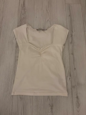 Ljusbeige topp med spets från 157 - Säljer en ljusbeige topp från 157 i storlek S. Toppen har korta ärmar, v-ringning med spetskant och en snygg rynkning framtill. Perfekt till jeans eller kjol för en enkel men söt look.