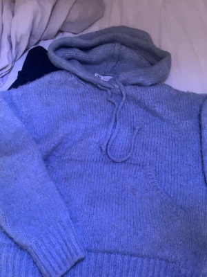 Ljusgrå stickad hoodie från Zara - Mysig ljusgrå stickad hoodie från Zara med huva och snörning. Tröjan har en stor magficka och ribbade muddar vid ärmslut och nederkant. Perfekt för kyliga dagar och enkel att styla med jeans eller leggings.