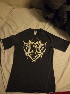 Gymshark svart t-shirt med tryck - Svart t-shirt från Gymshark i storlek M med unikt vitt grafiskt tryck fram och längs ryggen. Tillverkad i 88% återvunnen polyester och 12% elastan för en stretchig och bekväm passform. Perfekt för dig som gillar streetwear och gymmode. Säljs ej längre. Har aldrig använt den. Priset går att diskutera.