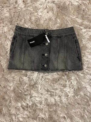 Grå jeanskjol från Weekday, strl 38 - Säljer en grå kort jeanskjol från Weekday i storlek 38. Kjolen har knappar framtill, rå kant nertill och markerade sömmar, helt oanvänd med lappen kvar. Denna kjol säljs även inte längre 