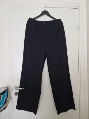 Amisu svarta vida kostymbyxor  - Säljer ett par Amisu svarta kostymbyxor med hög midja och vida ben. Byxorna har bälteshällor, knapp och dragkedja framtill samt två fickor bak. Perfekta för en clean och stilren look. Använda få gånger, fint skick. Storlek 42