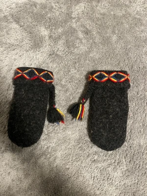 Svarta ullvantar Börjesson  - Säljer ett par svarta ullvantar från Börjesson storlek S. Vantarna har färgglada broderade detaljer i rött, gult och blått vid mudden samt tofsar i samma färger. Insidan är fodrad med Thinsulate för extra värme. Perfekta för kalla dagar!