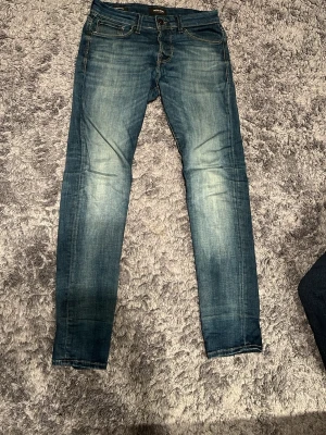 Jack & Jones Slim Glenn blå jeans - Säljer ett par Slim Glenn jeans från Jack & Jones i klassisk blå tvätt med snygga slitningar och kontrastsömmar. Modellen har fem fickor, smal passform och normal midja. Perfekta för dig som gillar en modern och clean look. Storlek 27/30.