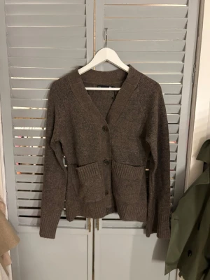 Brun kofta med fickor XS - Mysig brun kofta från lager 157 i storlek XS. Koftan har två stora fickor framtill, ribbade muddar och knäppning med knappar. Perfekt för lager-på-lager och chill dagar. Snygg och enkel att matcha med jeans eller kjol.