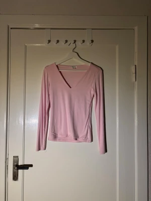 Ljusrosa långärmad topp med v-ringning - Säljer en ljusrosa långärmad topp med snygg v-ringning. Toppen är enkel och stilren, tillverkad i mjukt material som känns skönt mot huden. Perfekt att matcha med jeans eller kjol för en clean look.