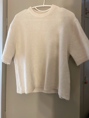 Vit stickad tröja från Gina Tricot - Kortärmad vit stickad tröja från Gina Tricot i storlek XS. Tröjan har ribbade kanter vid hals, ärmslut och nederkant. Perfekt för lager på lager och enkel att styla till olika looks. I nyskick 