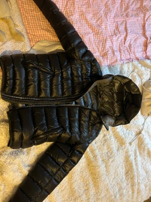 Svart pufferjacka från Colmar - Säljer en svart pufferjacka från Colmar med glansig finish och huva. Jackan har dragkedja framtill, två sidofickor med dragkedja och Colmar-logga på ärmen. Perfekt för kalla dagar och riktigt snygg till streetwear-stilen.