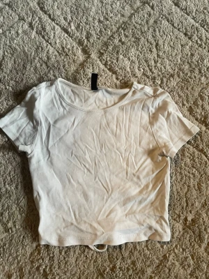Vit croppad t-shirt från H&M Divided - En basic vit croppad t-shirt från H&M Divided i storlek XS. T-shirten har korta ärmar och rund halsringning. Perfekt att matcha med jeans eller kjol för en clean och enkel look. Gjord i mjuk bomull som känns skön mot huden.