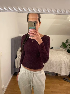 Vinröd stickad tröja från Gina Tricot - Mysig vinröd stickad tröja från Gina Tricot med kabelstickat mönster. Tröjan har en tight passform, långa ärmar och rundad halsringning. Perfekt till höst och vinter för en snygg och enkel look.