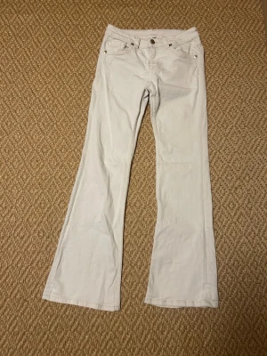 Vita bootcut jeans med fickdetaljer - Säljer ett super snygga par vita bootcut jeans med snygga fickdetaljer och guldfärgade nitar. Byxorna har klassisk femficksdesign och bakfickor med lock och knapp. Tillverkade i mjukt bomullstyg för en bekväm känsla och stilren look. 💕💕