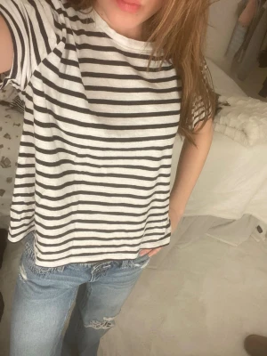 Randig vit och svart t-shirt - Säljer en loose fit t-shirt med svarta och vita horisontella ränder. Klassisk rund halsringning och korta ärmar. Skön och avslappnad passform, perfekt till jeans eller shorts. Materialet känns mjukt och andas, troligtvis bomull.