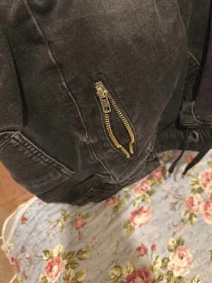 Svart bomberjacka med dragkedjor - Säljer en svart bomberjacka med coola detaljer som synliga dragkedjor i metall och snörning i midjan. Jackan har en klassisk bomberform och är tillverkad i ett slitstarkt material som ger en tuff look. Perfekt för dig som vill ha en streetstyle-vibe.