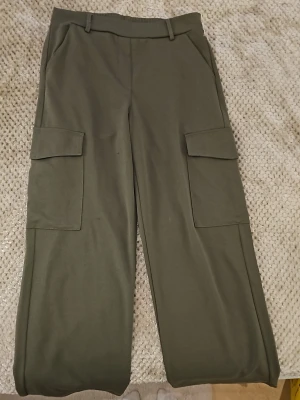 Olivgröna cargobyxor från Stories - Snygga olivgröna cargobyxor från Stories med raka ben och stora sidofickor. Byxorna har bälteshällor och är tillverkade i ett mjukt, stretchigt material som ger en avslappnad look. Perfekta för en trendig och bekväm stil.