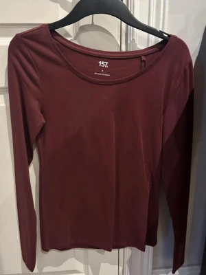 Vinröd långärmad topp från 157 - En enkel och stilren vinröd långärmad topp från 157. Toppen har rund halsringning och är gjord i mjuk bomull med en slim passform. Perfekt att matcha med jeans eller kjol för en clean look.