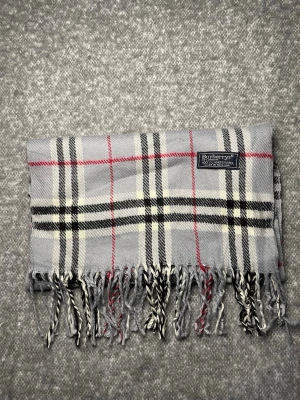 Burberry Halsduk Grå - Klassisk Burberry-halsduk i 100 % lammull. Mjuk och varm med tidlöst rutmönster i grått, svart, vitt och rött. Originaletikett, Made in England. 3G