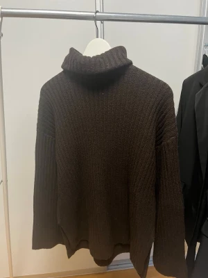 Brun polotröja i grovstickat - Mysig brun stickad polotröja med breda ribbade ärmar och hög krage. Oversized passform och mjukt material som passar perfekt för kyliga dagar. Enkel och stilren design utan synligt märke.