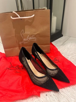 Svarta meshpumps från Christian Louboutin - Säljer ett par svarta pumps från Christian Louboutin med spetsig tå, meshdetaljer och små svarta nitar. Skorna har klassisk röd sula och transparent mesh med prickigt mönster. Perfekta för dig som vill sticka ut med exklusiv design.6 cm heels 
