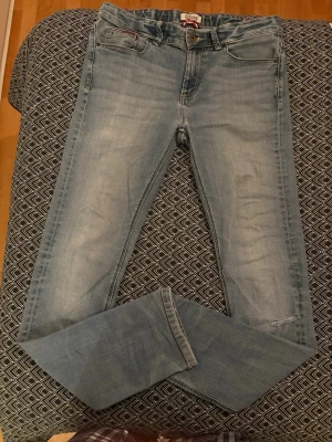 Tommy hilfiger ljusblå slim jeans - Snygga ljusblå jeans från Replay med klassisk femficksdesign och smal passform. Jeansen har diskreta slitningar och är tillverkade i mjukt denimtyg som ger en bekväm känsla. Perfekta för en avslappnad och trendig stil. Litet hål som syns vid slide 5