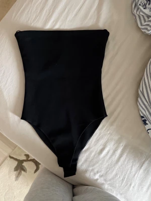 Svart body från Zara - En stilren svart body från Zara med enkel och klassisk design. Bodyn har raka linjer och hög skärning vid benen, perfekt för en trendig look på stranden eller vid poolen.