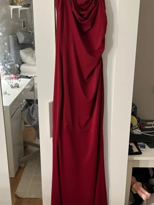 Vinröd långklänning från SHEIN - Säljer en elegant vinröd långklänning från SHEIN i storlek XS. Klänningen har draperad detalj framtill och är axelbandslös, vilket ger en snygg och stilren look. Perfekt för dig som vill sticka ut på nästa event!