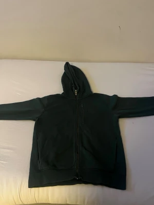 Mörkgrön hoodie med dragkedja - Snygg mörkgrön hoodie med dragkedja framtill och huva. Modellen har två fickor på sidorna och en extra ficka med dragkedja på bröstet. Perfekt för en avslappnad och cool stil. Materialet känns mjukt och bekvämt. Priset kan diskuteras 